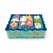 Angled view of a turquoise jewelry box covered in blue rhinestones, pearls, flowers, shells, a starfish and pastel ocean decorations.
