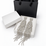 Close-up of silver rhinestone earrings with open geometric details and cascading crystal strands