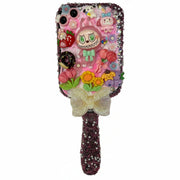Close up of a decoden paddle brush with a pink monster charm, colorful flowers, fruits, and sparkling crystals