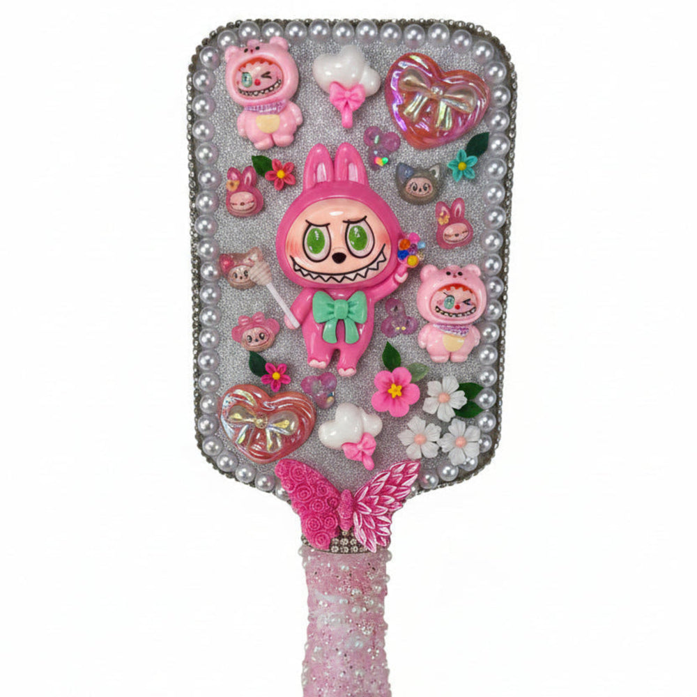 Close up of a decorated paddle brush with a cute pink monster, heart bow, butterfly, and shimmering finish.