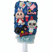 Close up of a decorated paddle brush with little monsters, smile charm, and glittering royal blue crystal stones