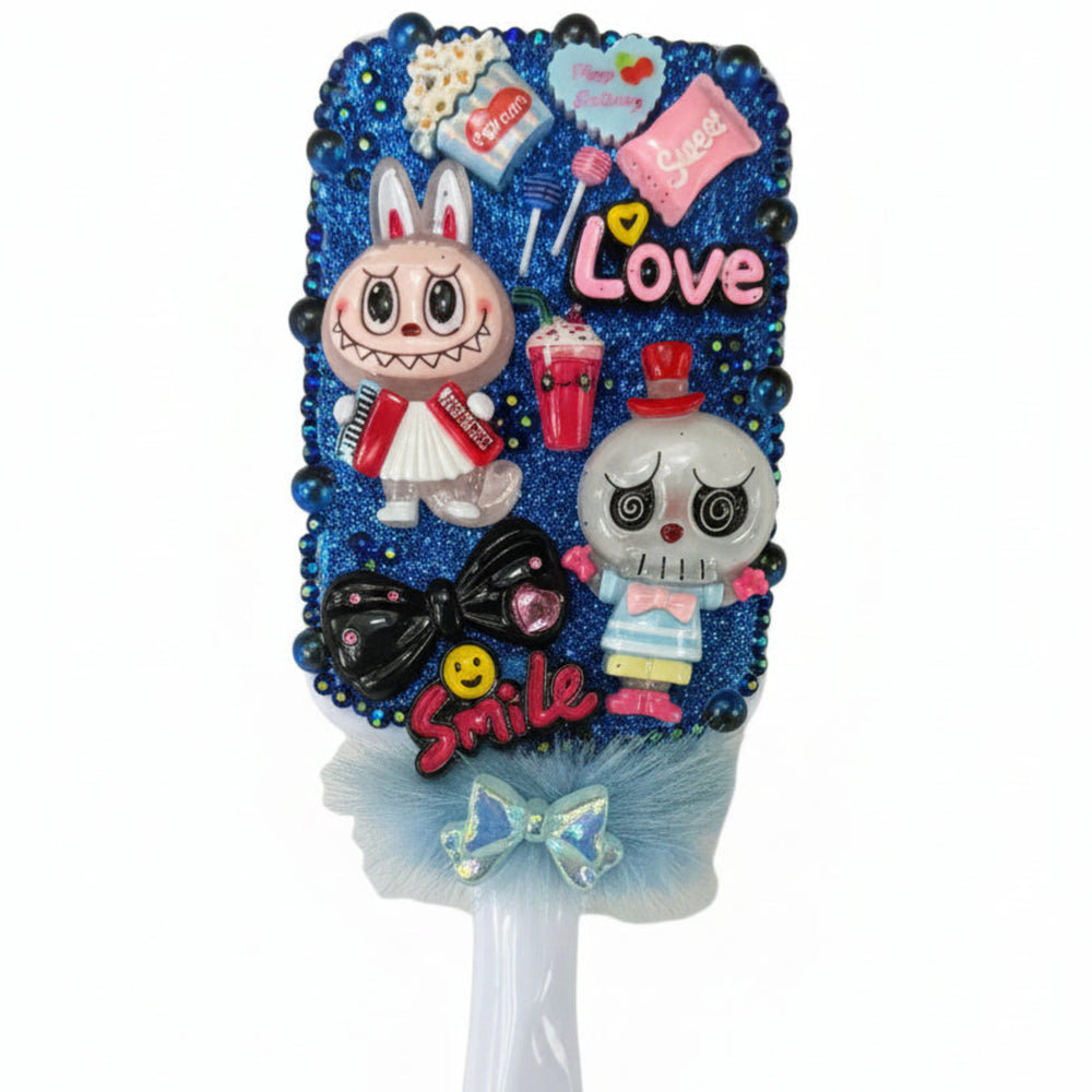 Close up of a decorated paddle brush with little monsters, smile charm, and glittering royal blue crystal stones