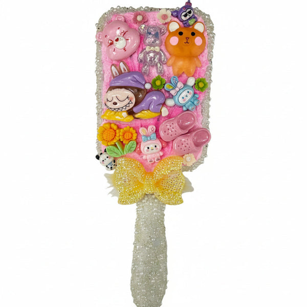 Close up of a decorated paddle brush with pink cream backing, mini pink crocs charms, butterfly, and heart details