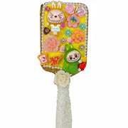 Close up of a handmade white paddle hair brush with a sparkling yellow glitter decoden base and cute monster charms