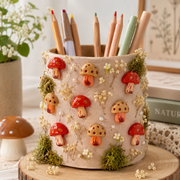 Decorative pencil cup embellished with red and beige mushroom charms, daisies, and greenery, shown as a creative DIY idea.