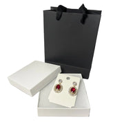 Elegant gold-tone earrings with ruby red gemstones displayed with premium gift box and black paper bag.