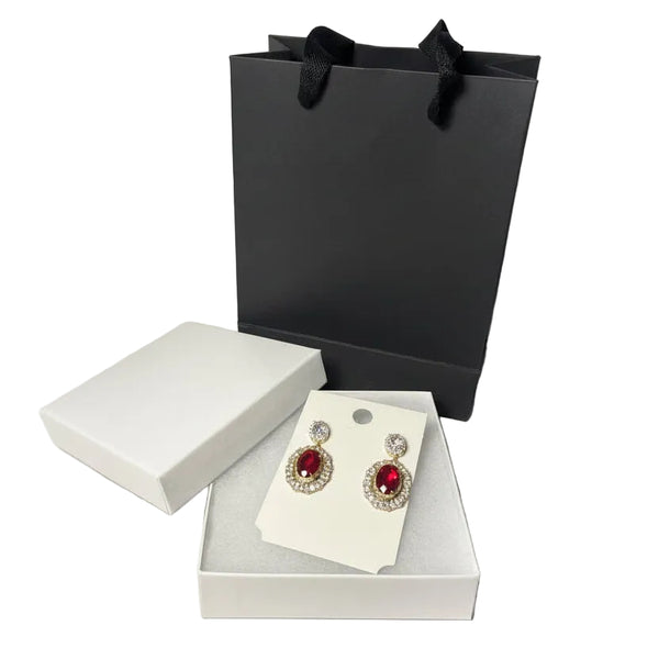 Elegant gold-tone earrings with ruby red gemstones displayed with premium gift box and black paper bag.