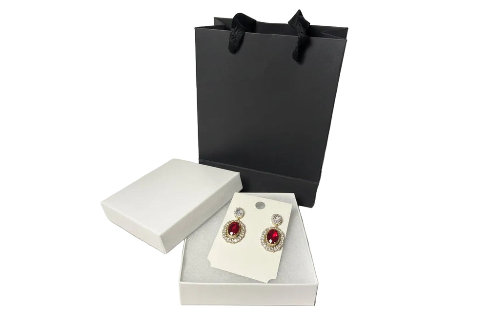 Elegant gold-tone earrings with ruby red gemstones displayed with premium gift box and black paper bag.