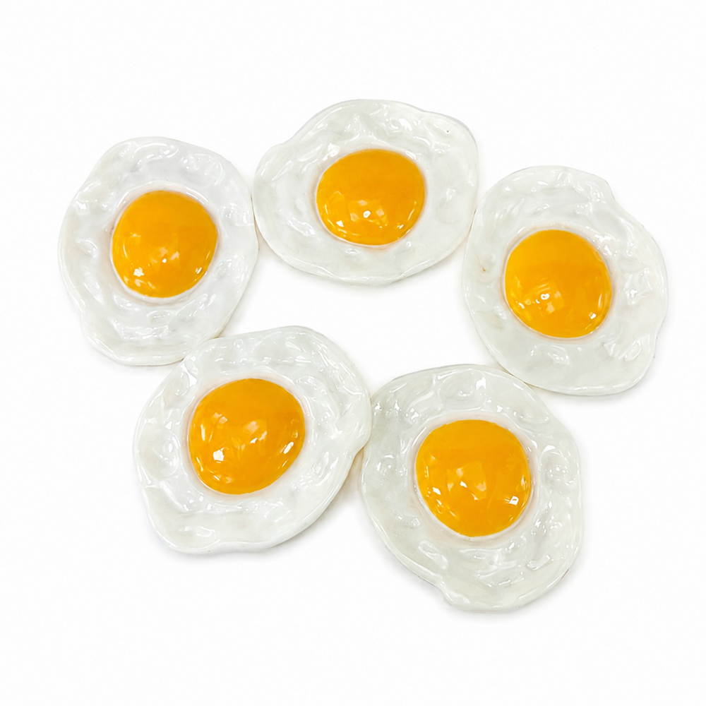 Five mini plastic toy fried eggs arranged on a plain white background.