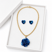 Gold-tone blue rose necklace with matching crystal heart earrings displayed in an elegant white jewelry box.