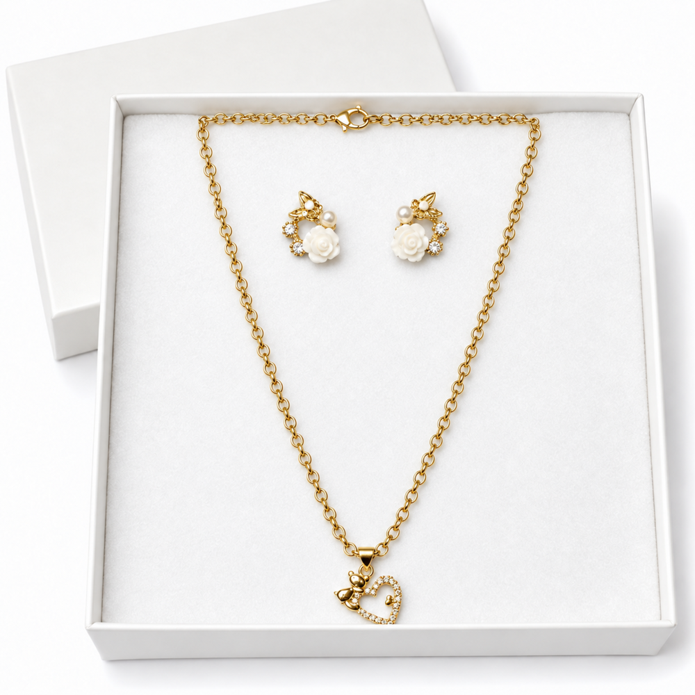 Gold necklace and matching stud earrings displayed in a white gift box. The necklace has a delicate gold chain with a small heart-shaped pendant, and the earrings feature white rose motifs with small clear stones.