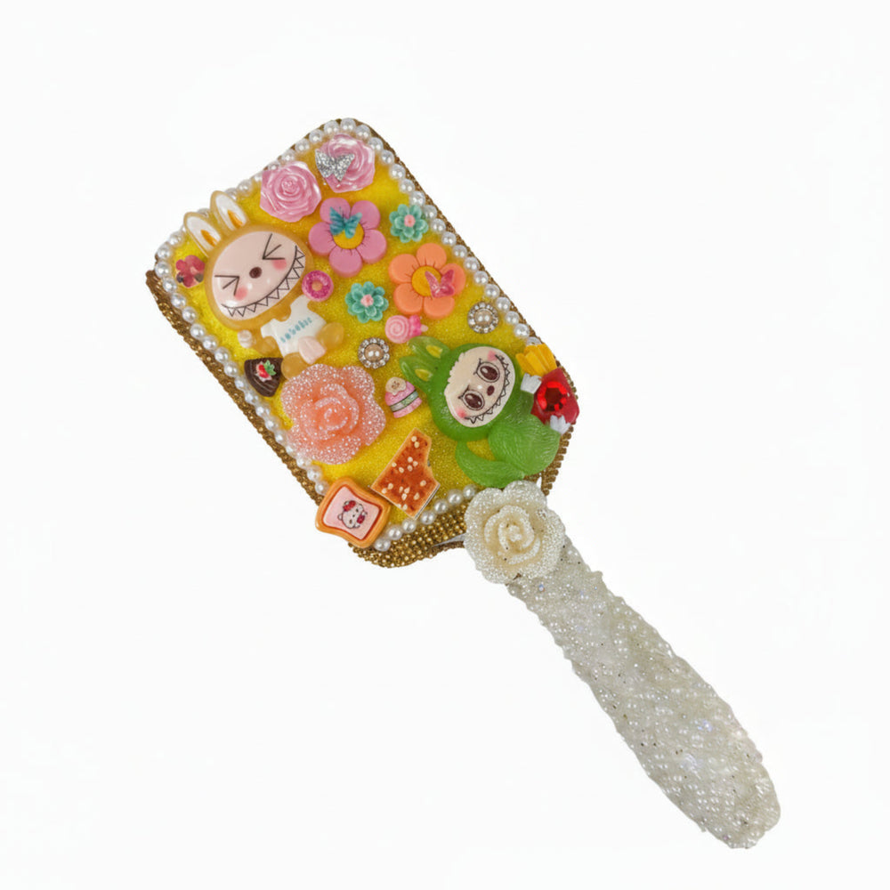 Handmade white decoden hair brush featuring pink roses, colorful mini flowers, and a glittery rose accent on a yellow base