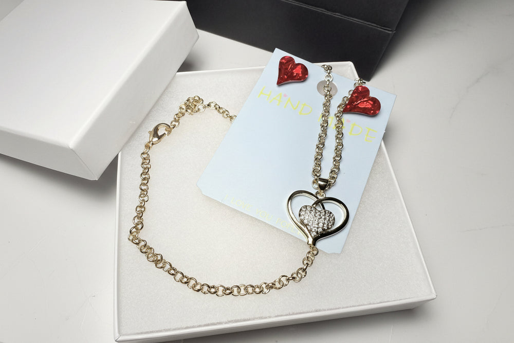 Red crystal earrings and gold-tone heart pendant necklace displayed in a white gift box with a luxury black gift bag and red heart crystal earrings