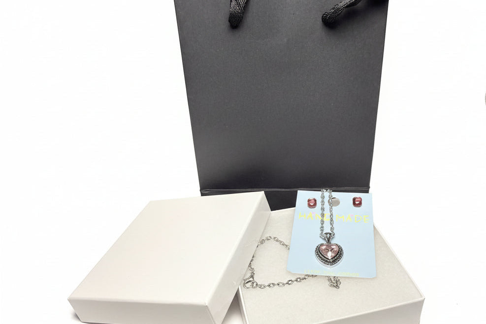 Close-up of a sparkling pink heart pendant necklace and crystal earring set, on a white jewelry card, displayed with a premium gift box
