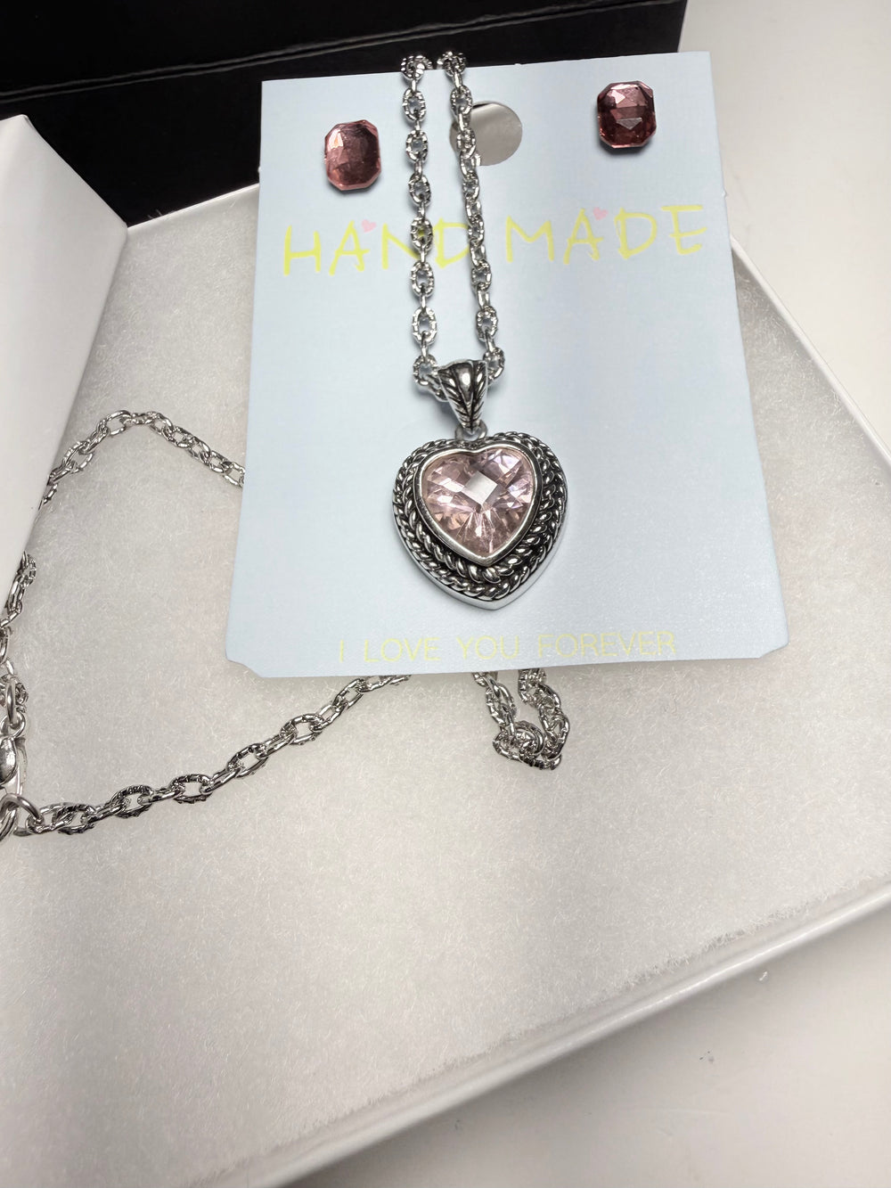 Heart-shaped pendant necklace and earrings on a 'Handmade' card with a white background
