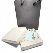 Detailed close-up of a sparkling gold-tone heart pendant necklace and matching earrings, presented in a luxury gift box with a grey gift bag