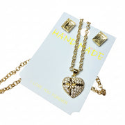 Detailed close-up of a sparkling gold-tone heart pendant necklace and matching earrings, presented in a luxury gift box with a grey gift bag.