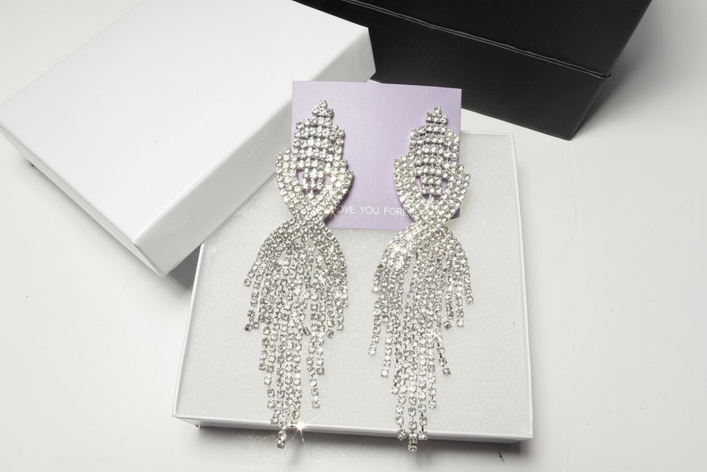 Close-up of sparkling silver-tone teardrop earrings on a white jewelry box - Premium detail