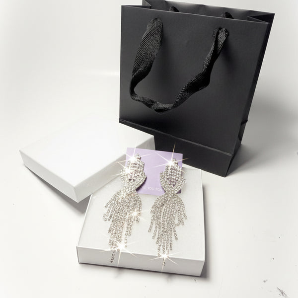 Luxury fringe teardrop crystal earrings displayed on a white gift box next to a black paper bag - elegant gift-ready jewelry presentation.