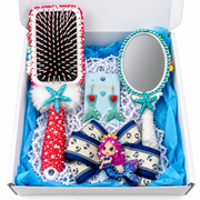Mermaid-themed gift box with decorated hairbrush, pearl-trimmed mirror, mermaid tail earrings, and navy anchor bow with doll charm.