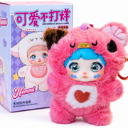 Pink Nommi plush keychain with bright blue hair, heart chest detail, gold ring, and Loveliness Never Ends collectible box.