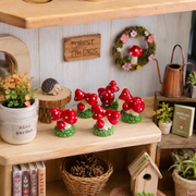 Red mushroom miniatures displayed in a succulent terrarium with moss, stones and small plants