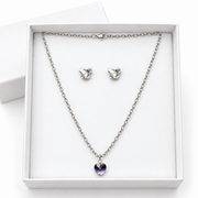 Silver-tone chain necklace and matching stud earrings set in a white gift box. The necklace has a heart-shaped purple crystal pendant, and the matching earrings have heart-shaped iridescent clear crystals.