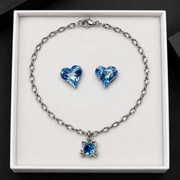Silver cat pendant necklace with blue heart earrings arranged on a white jewelry box insert