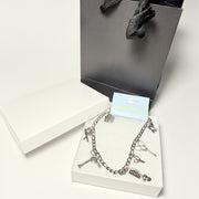 Silver charm anklet for hairdressers featuring scissor and comb pendants, displayed on a white gift box with a black luxury gift bag 