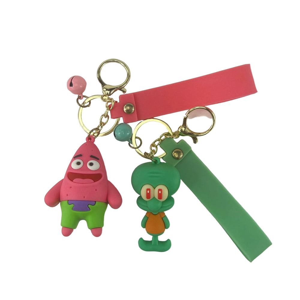 Two cartoon character keychains with wristlet straps on a white surface. One keychain features a pink starfish character with green pants and a pink strap.