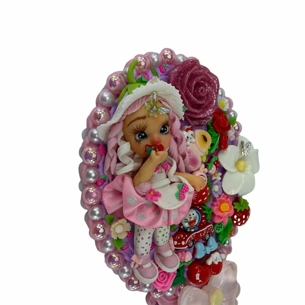 close-up of a pink decoden mirror back filled with miniature strawberry charms, resin roses, and a small doll
