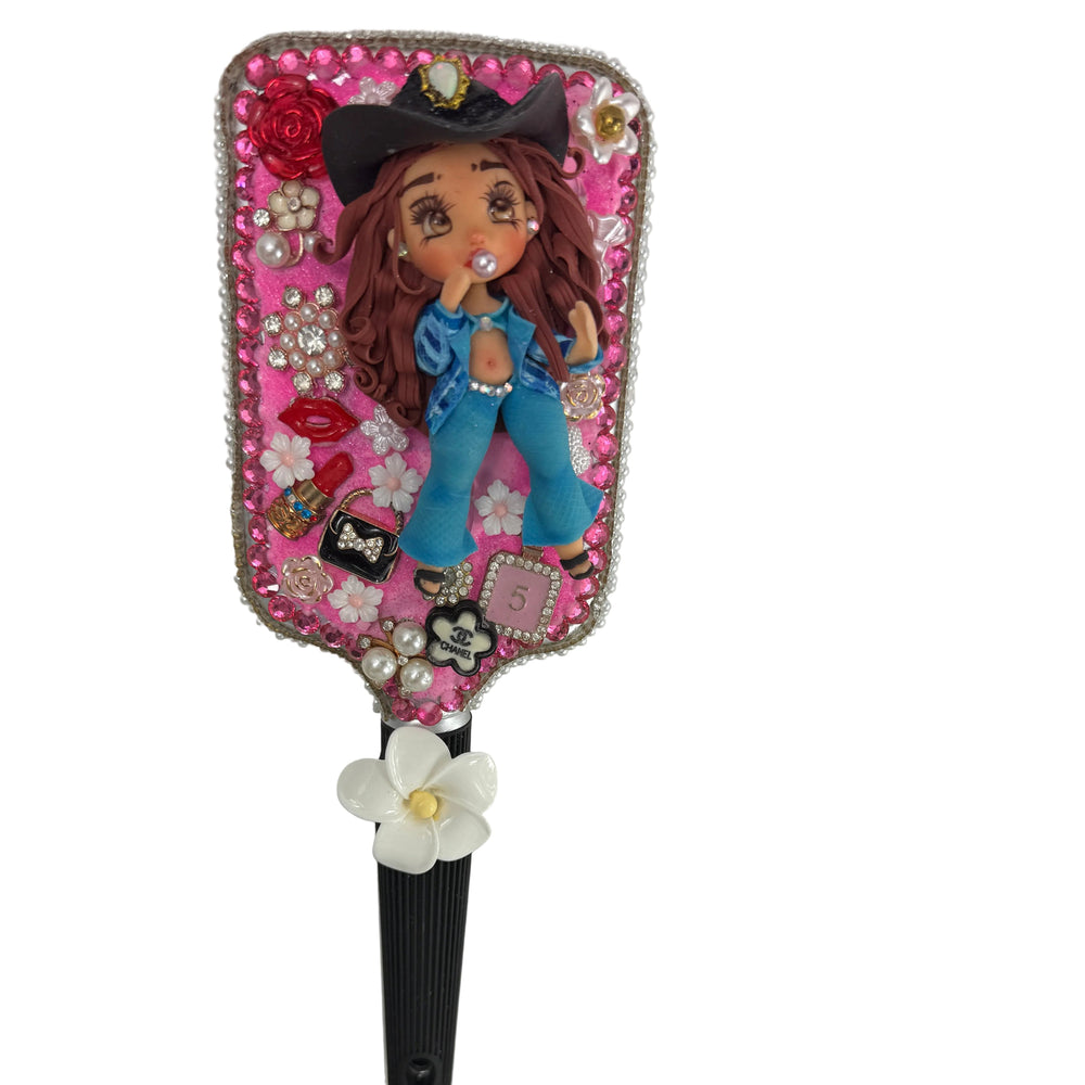 close up design of a handmade decoden hair brush decorated with a cowgirl figure flowers and sparkles
