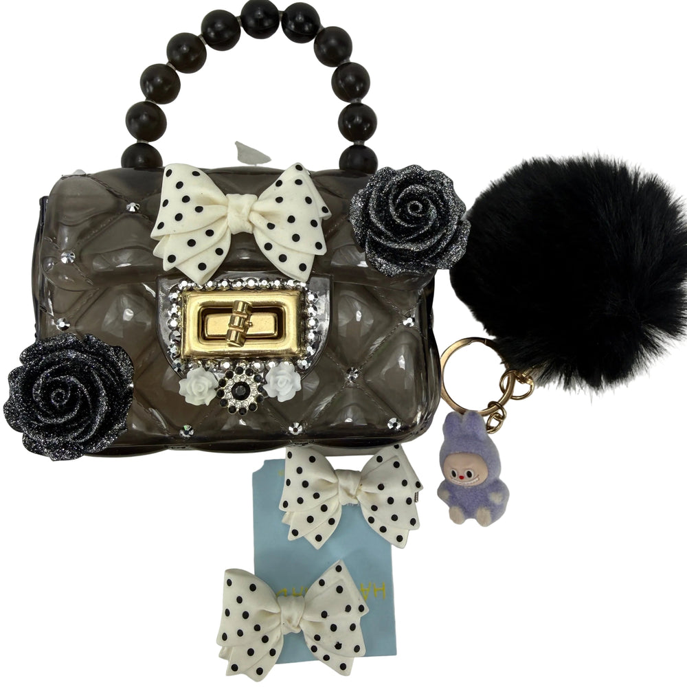 dark small purse with black pompom and roses, next to decorative hair bows