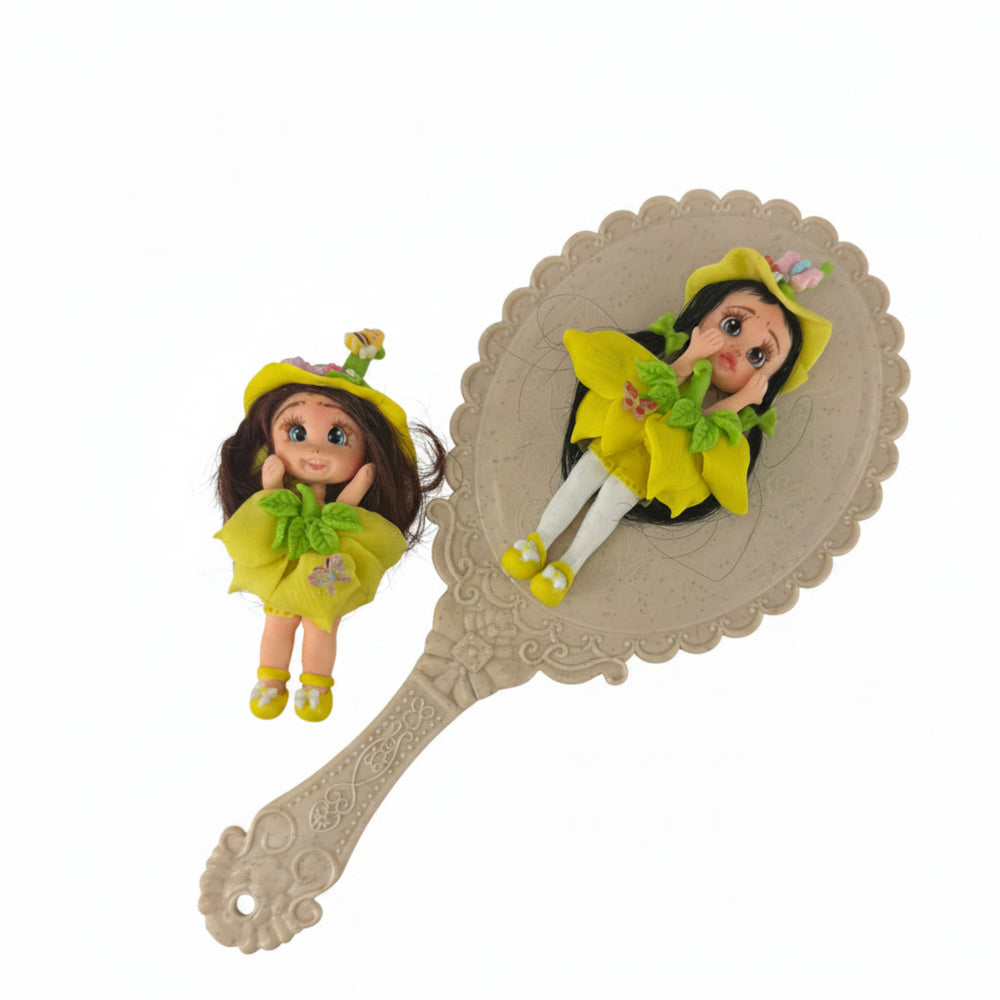 fairy flex porcelain doll with yellow outfit and green flowers next to a decorative hand mirror 