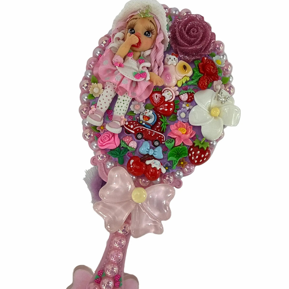 pink hand mirror decorated with decoden whipped cream, strawberry charms, coquette bows, and a handmade doll